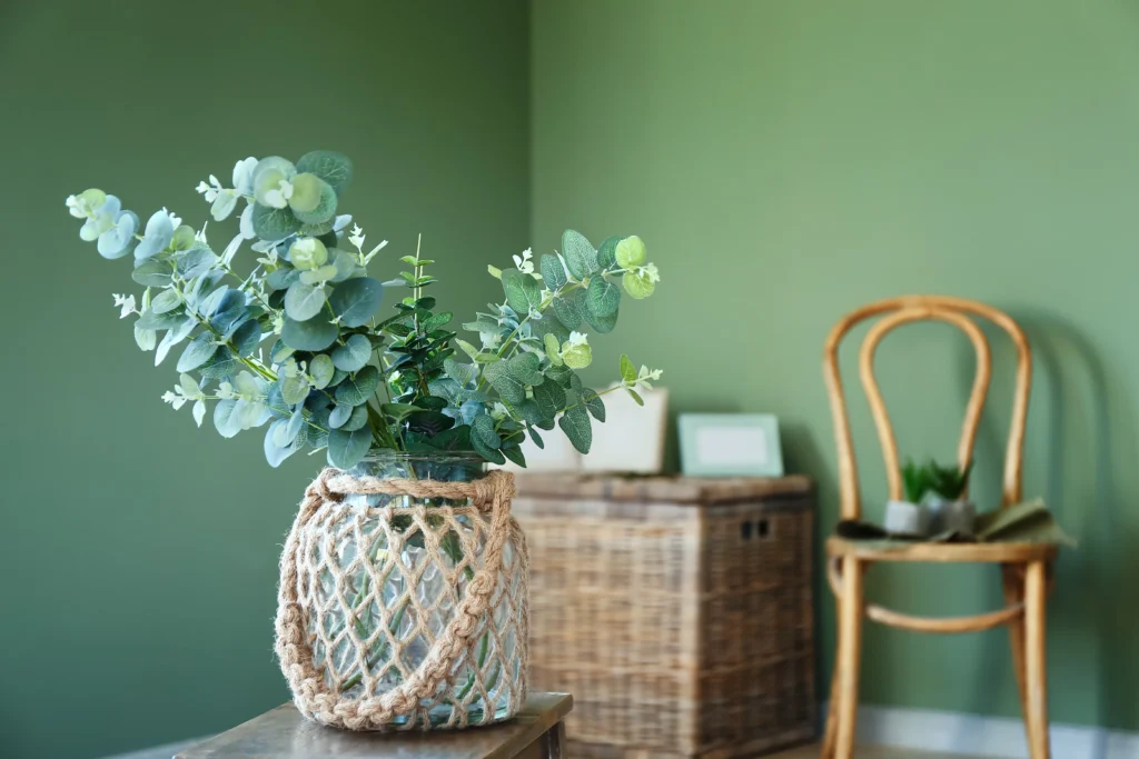 Florero de cristal con ramas de eucalipto en una habitacion verde de Tendencias en Diseno de Interiores 2026.
