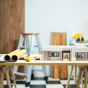 Cómo remodelar una casa: fotografía de la maqueta de una casa de un piso y a lado planos enrollados.